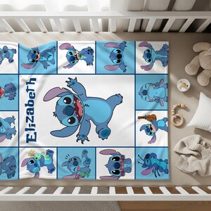 May include: A baby blanket featuring a blue and white design with the character Stitch from Lilo & Stitch. The blanket has a grid pattern with various Stitch poses and the name "Elizabeth" in blue. The blanket is in a crib with a teddy bear and other baby items.