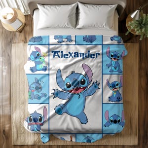 May include: A blue and white blanket featuring the character Stitch from Lilo & Stitch. The blanket has a grid pattern with various Stitch poses and the name "Alexander" in blue text. The blanket is on a bed with white pillows.