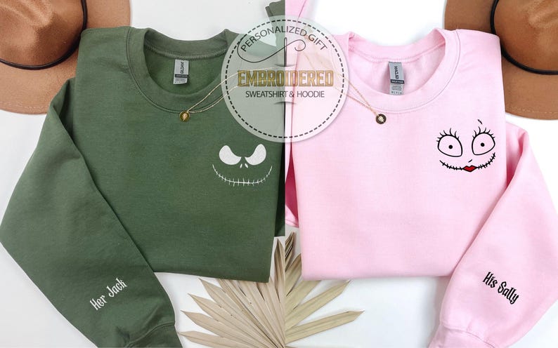 May include: Two sweatshirts, one olive green and one pink, with embroidered character faces. The green sweatshirt has "Her Jack" on the sleeve, and the pink one has "His Sally." Both have gold necklaces and the text "EMBROIDERED SWEATSHIRT & HOODIE".