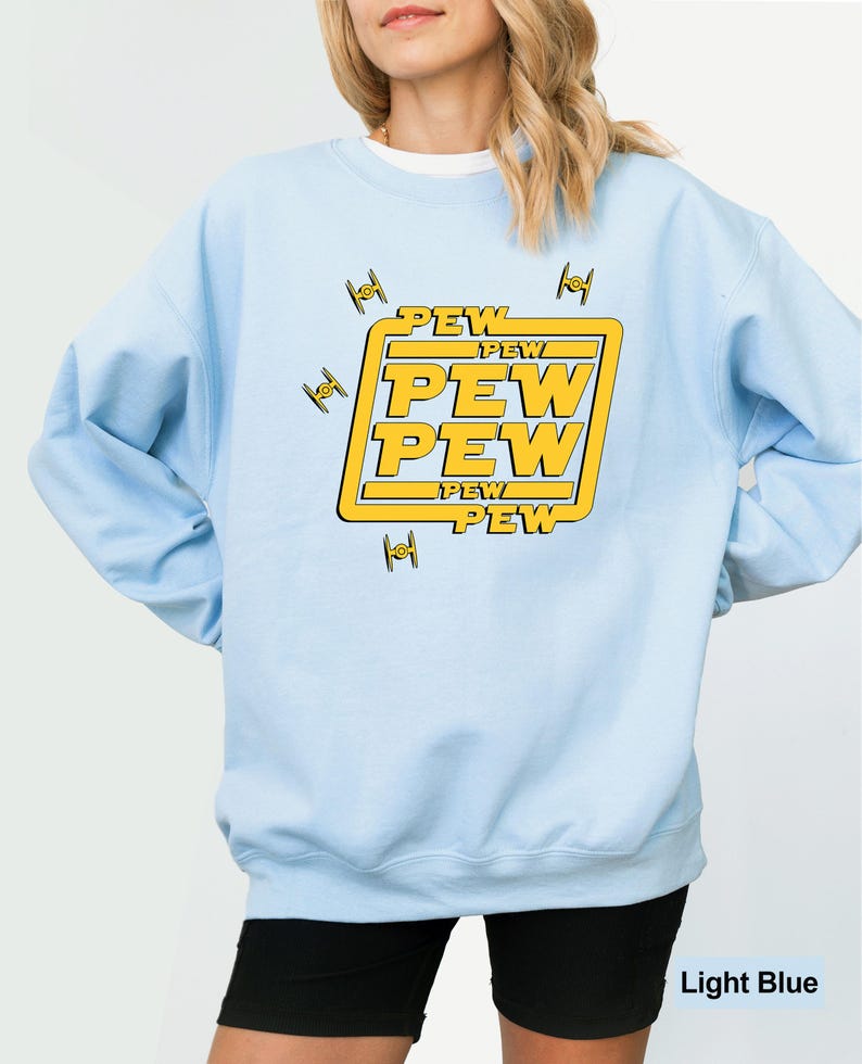 May include: Light blue sweatshirt with a yellow graphic that says "PEW PEW PEW" in a bold font. The design includes small, stylized spaceship illustrations. The sweatshirt is a solid light blue color.
