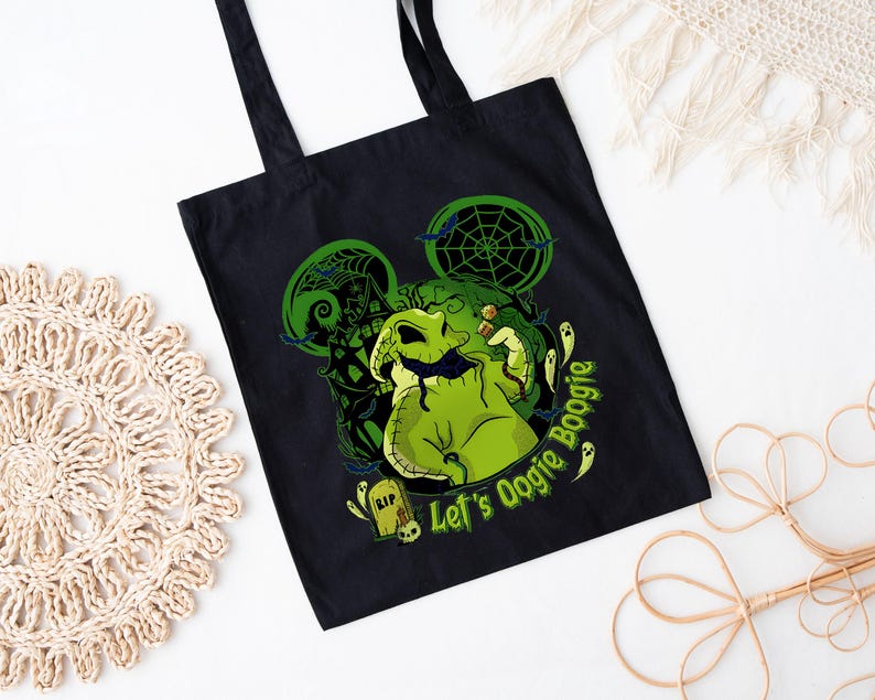 Op de afbeelding: Zwarte draagtas met een groene Oogie Boogie-afbeelding en de tekst "Let's Oogie Boogie". Het ontwerp bevat een spinnenweb, geesten en een grafsteen. De tas heeft twee zwarte handvatten.