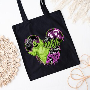 May include: Black tote bag with a green Oogie Boogie character design and the text "Let's Oogie Boogie" in green and white. The design includes purple and pink accents, spiderwebs, and skulls. The bag has black handles.