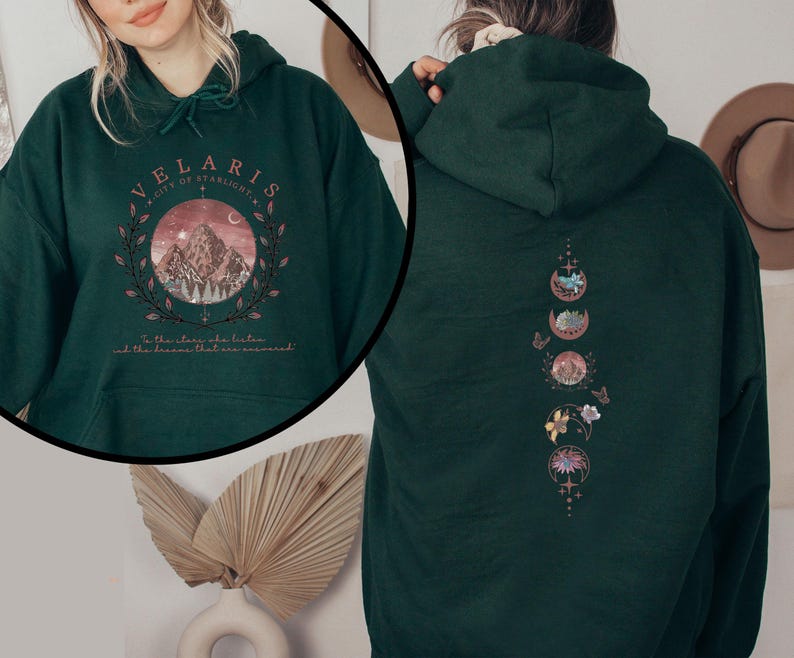 May include: Dark green hoodie with a front graphic featuring a mountain scene within a circle, the text "VELARIS CITY OF STARLIGHT", and the quote "To the stars who listen and the dreams that are answered." The back has a vertical design of moon phases.