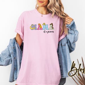 K&ouml;nnte beinhalten: Pinkes T-Shirt mit einem Aufdruck von Disney-Prinzessinnen, die "MAMA of a princess" buchstabieren.