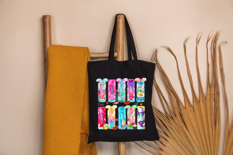 Pu&ograve; includere: Borsa tote nera con illustrazioni colorate di lattine di bevande con vari disegni. Le lattine hanno colori vivaci e temi tropicali. La borsa &egrave; appesa a una scala di legno.