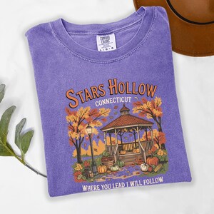May include: A purple Comfort Colors t-shirt featuring a graphic of a gazebo in autumn with the text "Stars Hollow Connecticut" and "Where You Lead I Will Follow". The design includes pumpkins, trees, and a lamppost.