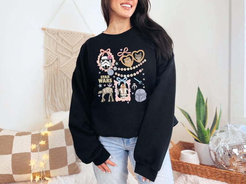 May include: Black sweatshirt featuring Star Wars characters in decorative frames. The design includes images of a Stormtrooper, Ewoks, R2-D2, and a Mandalorian helmet, with the words "Star Wars" in the center.