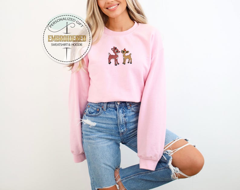 Peut inclure: Un sweat-shirt rose avec une image brod&eacute;e de deux cerfs de dessin anim&eacute;. Le sweat-shirt est port&eacute; par une personne aux cheveux longs blonds et un jean bleu.