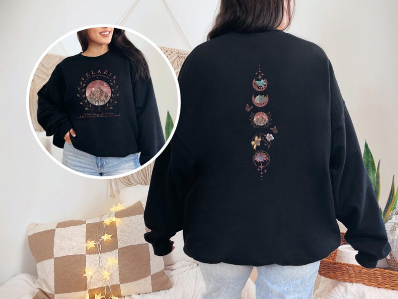 May include: Black sweatshirt with a circular graphic on the front featuring a mountain scene and the word "Velaris". The back of the sweatshirt has a vertical design of moon phases, flowers, and butterflies in shades of pink and gold.