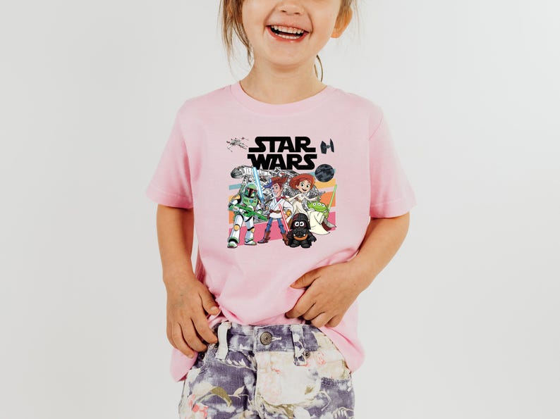 Puede incluir: Camiseta rosa de manga corta con un gr&aacute;fico colorido de personajes de Star Wars. El dise&ntilde;o incluye el logotipo de Star Wars y varias figuras de dibujos animados de la franquicia. La camiseta la lleva un ni&ntilde;o.