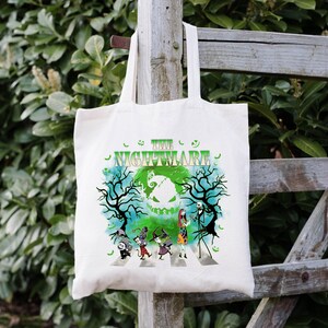 Pode incluir: Saco tote branco sujo com um gr&aacute;fico colorido de "O Estranho Mundo de Jack". O design inclui Jack Skellington, Sally e outros personagens atravessando uma faixa de pedestres, com o t&iacute;tulo em verde.