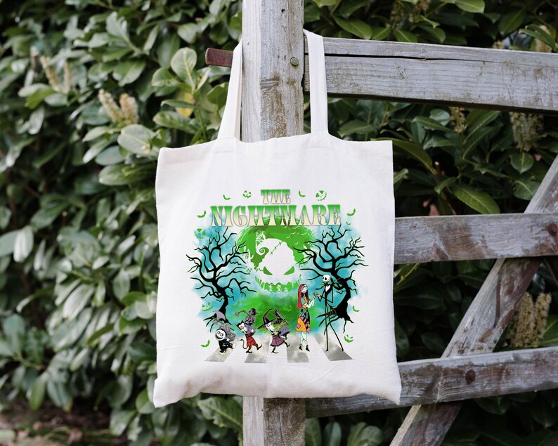Pode incluir: Saco tote branco sujo com um gr&aacute;fico colorido de "O Estranho Mundo de Jack". O design inclui Jack Skellington, Sally e outros personagens atravessando uma faixa de pedestres, com o t&iacute;tulo em verde.