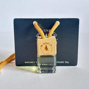 May include: A small, clear glass bottle with a wooden cap that says "Bel Scents Co." and has a small leaf design. The bottle is hanging from a yellow cord and is labeled "Whiskey Sour Hanging Diffuser 10g".