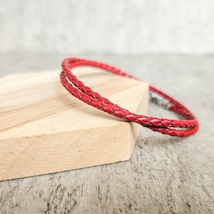 Puede incluir: Un collar de cuero trenzado rojo con un cierre plateado.