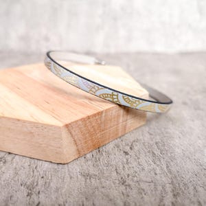 Könnte beinhalten: Ein dünnes silbernes Armkettchen mit einem weißen und goldenen Muster.