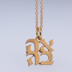 May include: Gold chain necklace with a pendant featuring the letters "RS" in a stylised, gothic font.