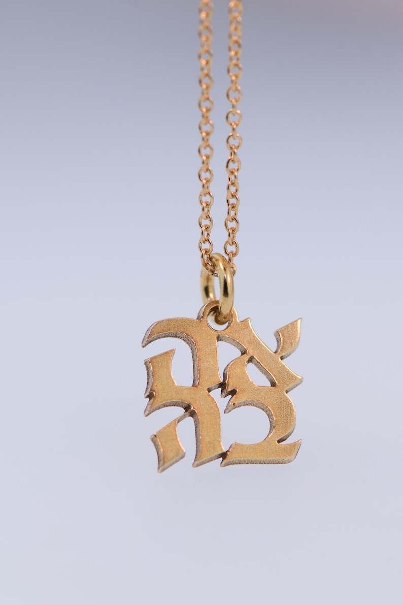 May include: Gold chain necklace with a pendant featuring the letters "RS" in a stylised, gothic font.