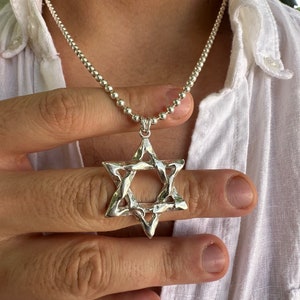 Puede incluir: Un collar de cadena de plata con un gran colgante de plata en forma de Estrella de David.