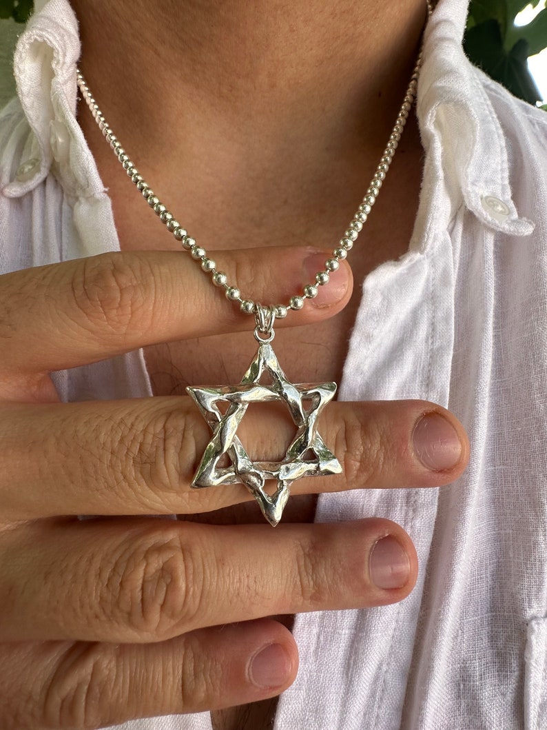 Puede incluir: Un collar de cadena de plata con un gran colgante de plata en forma de Estrella de David.
