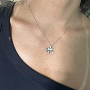Puede incluir: Un collar de cadena de plata con un colgante que presenta la letra hebrea 'Chai' (vida).