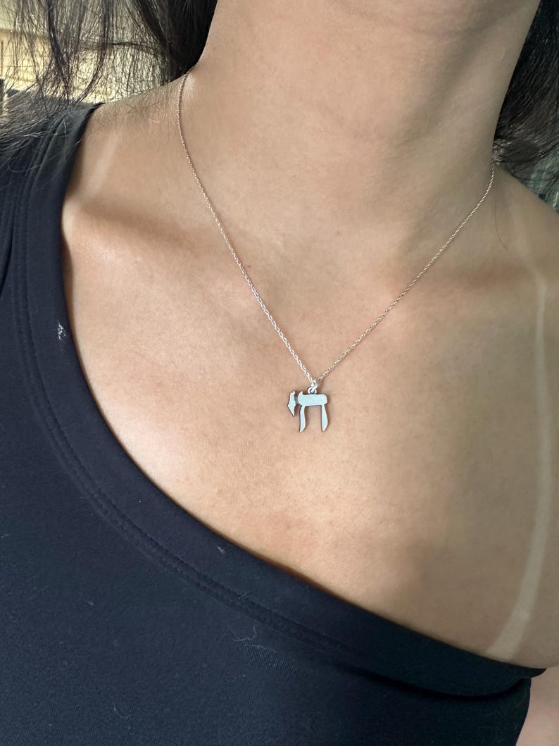 Puede incluir: Un collar de cadena de plata con un colgante que presenta la letra hebrea 'Chai' (vida).