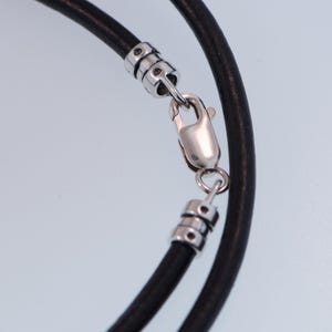 Pu&ograve; includere: Primo piano di una collana in pelle nera con chiusura color argento. La collana &egrave; composta da due fili di pelle nera e presenta una chiusura a moschettone per una chiusura sicura. I dettagli in metallo aggiungono un tocco di eleganza.