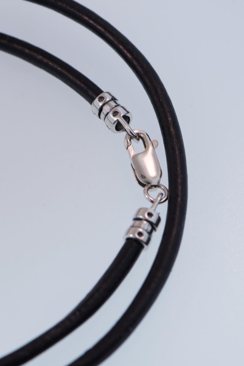 Pu&ograve; includere: Primo piano di una collana in pelle nera con chiusura color argento. La collana &egrave; composta da due fili di pelle nera e presenta una chiusura a moschettone per una chiusura sicura. I dettagli in metallo aggiungono un tocco di eleganza.