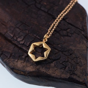 May include: A gold chain necklace with a hexagonal pendant featuring a star-shaped cutout. The pendant is on a dark brown wooden surface.