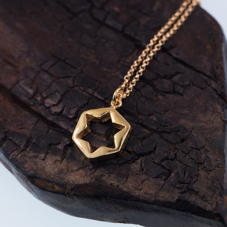 May include: A gold chain necklace with a hexagonal pendant featuring a star-shaped cutout. The pendant is on a dark brown wooden surface.