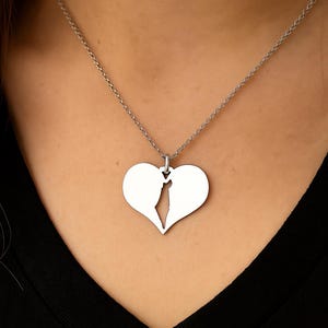 Op de afbeelding: Een zilverkleurige ketting met een hartvormige hanger, in twee helften gesplitst. De hanger hangt aan een fijne ketting. De ketting wordt gepresenteerd tegen een donkere achtergrond.