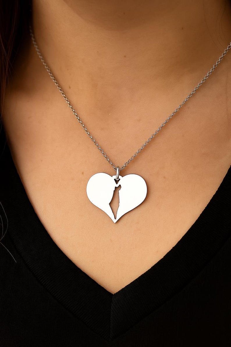 Op de afbeelding: Een zilverkleurige ketting met een hartvormige hanger, in twee helften gesplitst. De hanger hangt aan een fijne ketting. De ketting wordt gepresenteerd tegen een donkere achtergrond.