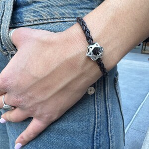 May include: A brown leather braided bracelet with a silver Star of David charm.