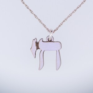 Puede incluir: Un collar de cadena de plata con un colgante de esmalte blanco en forma de la letra hebrea Jai.