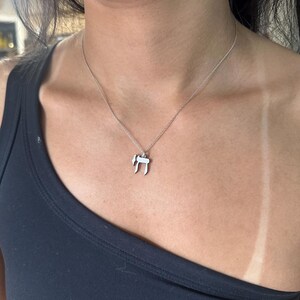 Puede incluir: Un collar de cadena de plata con un peque&ntilde;o colgante de plata con la letra hebrea 'Chai'.