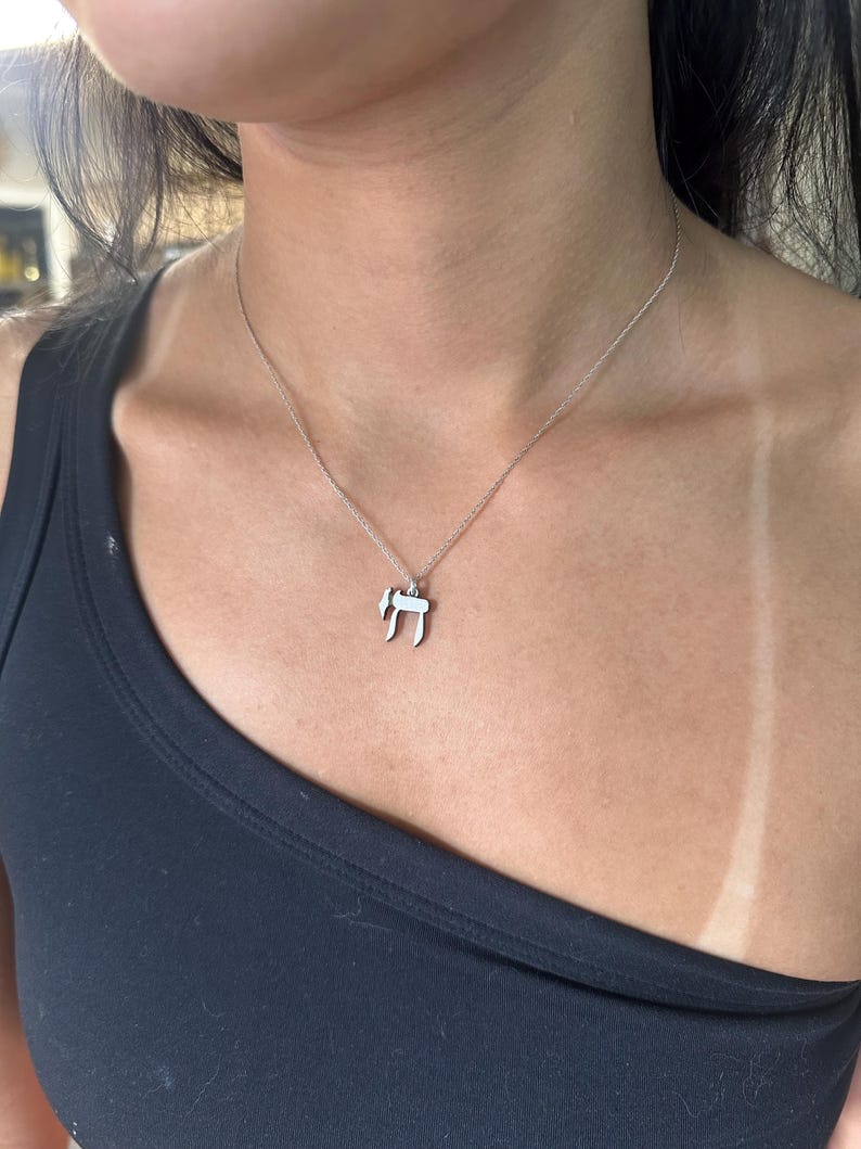 Puede incluir: Un collar de cadena de plata con un peque&ntilde;o colgante de plata con la letra hebrea 'Chai'.