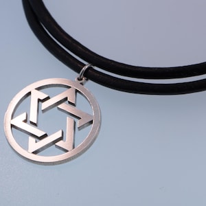 Pu&ograve; includere: Un ciondolo color argento con un design a Stella di David, sospeso a una collana con cordino in pelle nera. Il ciondolo &egrave; circolare con una stella a sei punte ritagliata. La collana &egrave; esposta su uno sfondo azzurro.