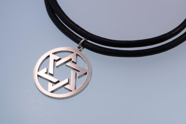 Pu&ograve; includere: Un ciondolo color argento con un design a Stella di David, sospeso a una collana con cordino in pelle nera. Il ciondolo &egrave; circolare con una stella a sei punte ritagliata. La collana &egrave; esposta su uno sfondo azzurro.