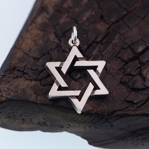 May include: A silver Star of David pendant with a geometric design. The pendant is on a dark brown wooden surface.