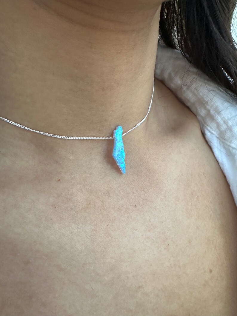 Op de afbeelding: Een zilveren ketting met een blauwe opaal hanger. De opaal is druppelvormig en heeft een iriserende glans.