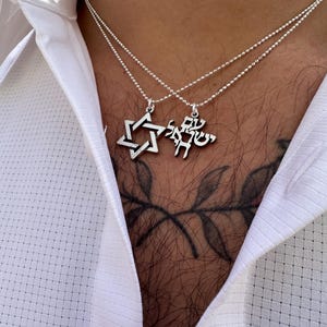 Puede incluir: Un collar de cadena de plata con dos colgantes. Un colgante es una estrella de David y el otro es una inscripci&oacute;n en hebreo.