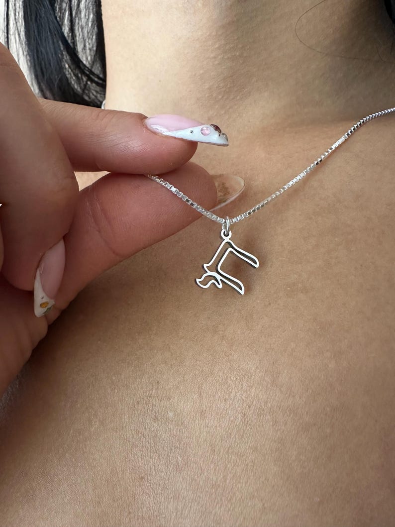 Peut inclure: Un collier argent&eacute; avec un pendentif d&eacute;licat en forme de la lettre "R". Le pendentif est suspendu &agrave; une fine cha&icirc;ne. Le collier est pr&eacute;sent&eacute; sur un fond de teint.