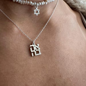 May include: Two silver necklaces with pendants. The top necklace is a pearl choker with a silver Star of David pendant. The bottom necklace has a silver pendant with a Hebrew letter.