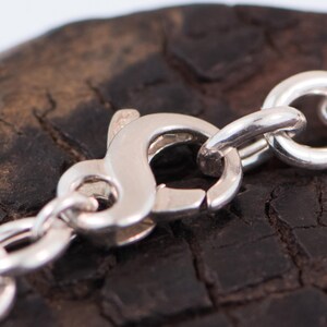 May include: A silver chain necklace featuring a polished lobster claw clasp. The metal links are round and interconnected, creating a continuous loop. The clasp mechanism is visible in the centre, showing the spring-loaded lever and the hook.