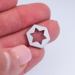 May include: A silver-colored metal charm in the shape of a six-pointed star with a smaller star cut out in the center.