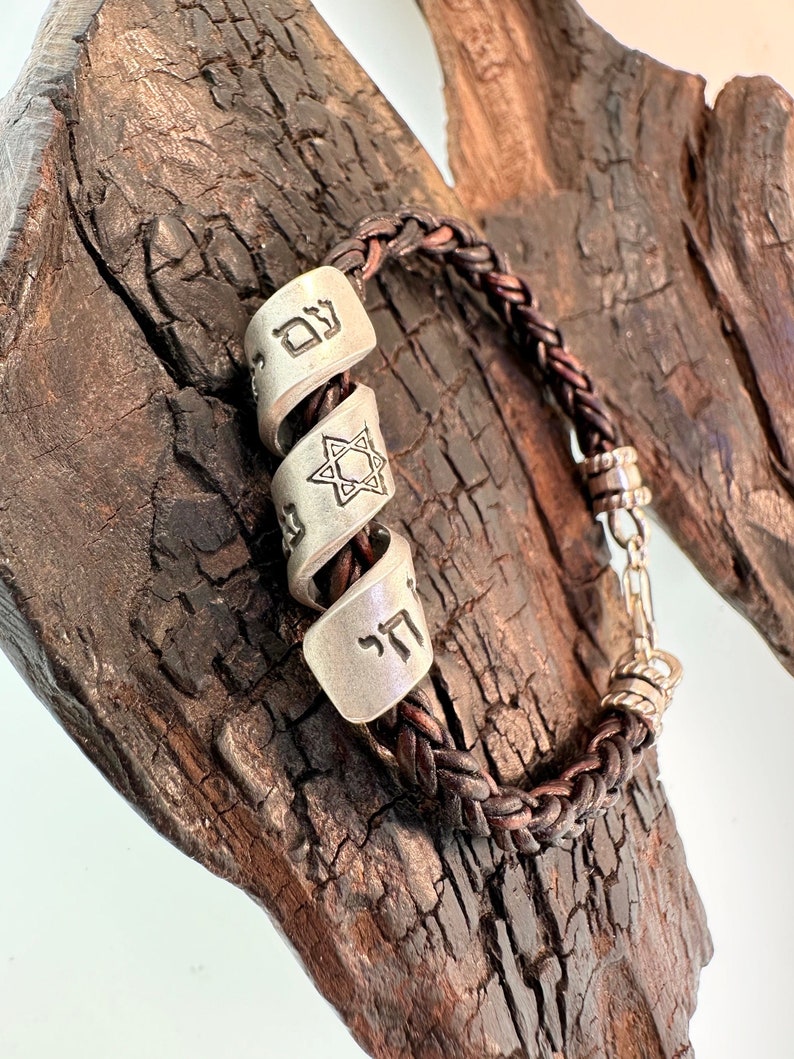 May include: A brown leather braided bracelet with silver charms. The charms feature Hebrew lettering and a Star of David.