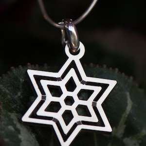 May include: A silver-colored pendant necklace featuring a six-pointed star design. The star has a geometric pattern with a central hexagon and surrounding diamond shapes. The pendant hangs from a thin, silver chain.