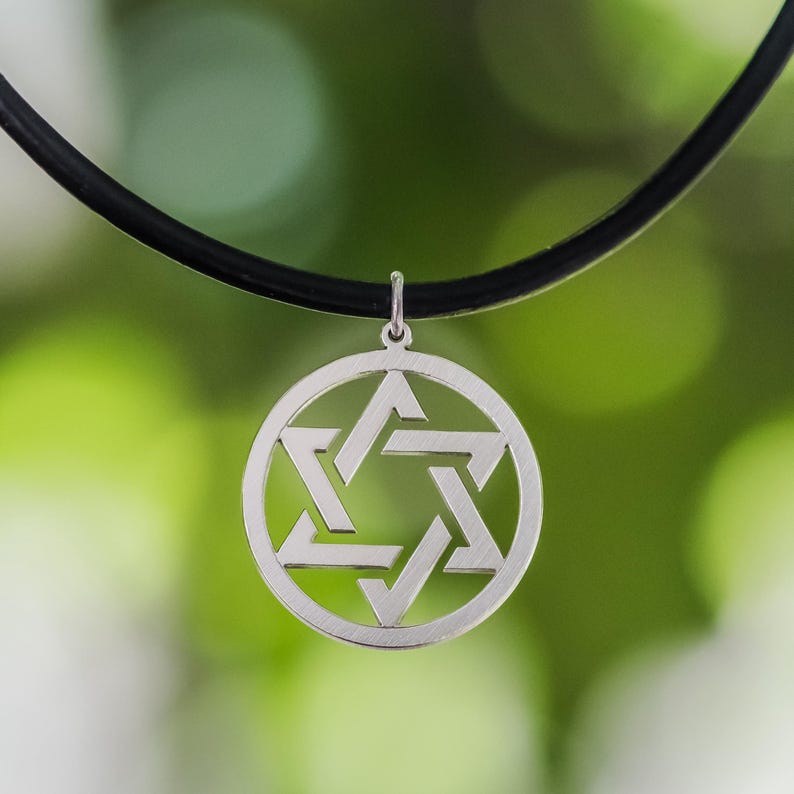 Pu&ograve; includere: Un ciondolo color argento con un design a Stella di David, sospeso a un cordino nero. Il ciondolo &egrave; circolare, con la stella a sei punte al centro. Lo sfondo &egrave; un verde sfocato.