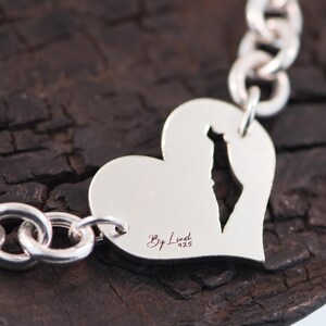 May include: A silver chain bracelet featuring a heart-shaped charm with a cutout in the shape of Israel. The charm is engraved with the text By Linet 925. The bracelet is constructed from polished silver links connected to the heart charm.