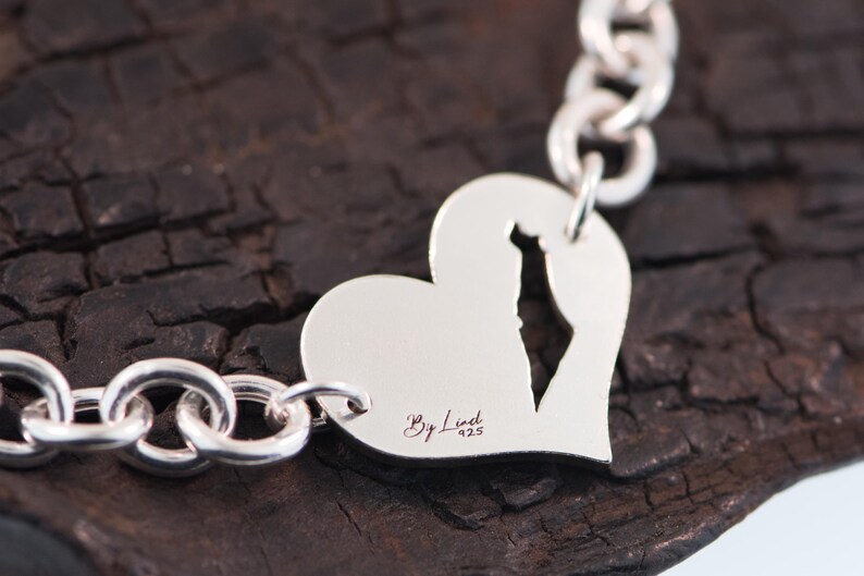 May include: A silver chain bracelet featuring a heart-shaped charm with a cutout in the shape of Israel. The charm is engraved with the text By Linet 925. The bracelet is constructed from polished silver links connected to the heart charm.