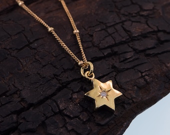 Puede incluir: Un collar de cadena dorada con un pequeño colgante de estrella con una piedra preciosa transparente en el centro.